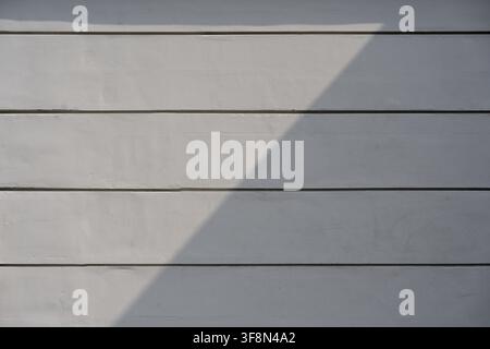 Light grey wall texture with horizontal grooves featuring a sharp diagonal shadow cast across the surface. Stock Photo