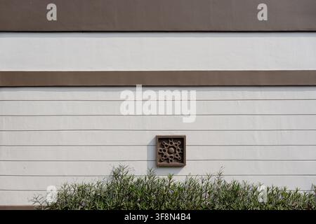 White grooved wall with brown architectural bands and a decorative square tile above green plants. Stock Photo