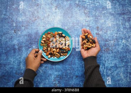 Hands holding mixed nuts with a plate of nuts nearby Stock Photo