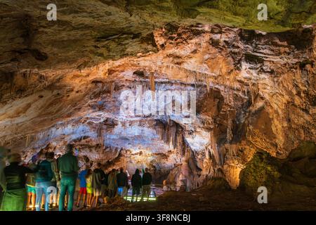 A group of visitors stands on a walkway inside Lipa Cave in Montenegro, observing dramatic limestone formations. The large cavern is filled with stala Stock Photo