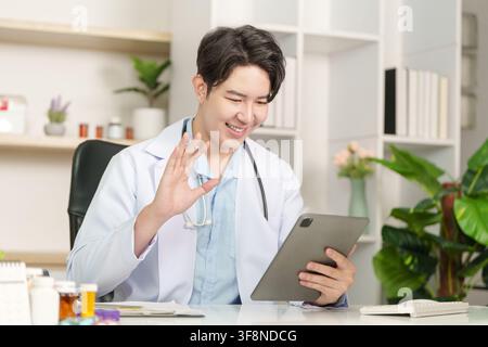 Asian male doctor waving on video call using digital tablet for telehealth consultation Stock Photo