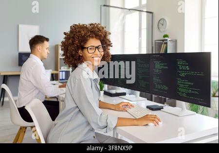Smiling woman programmer working on code at desktop in bright tech office Stock Photo