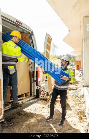 Two builders in high visibility jackets unloading blue pipes Stock Photo