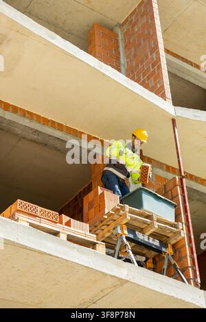 Smiling mason worker holding brick and trowel on scaffolding Stock Photo