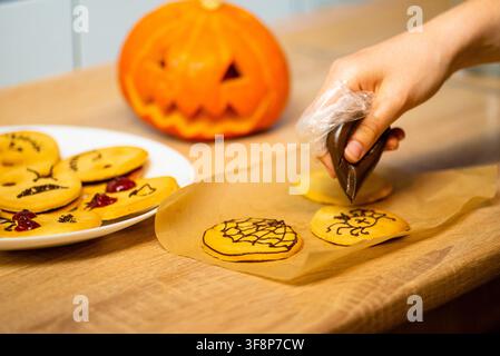 Process of drawing chocolate faces on holiday biscuits on a wooden table with blurred background jack o lantern Stock Photo