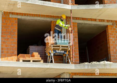 Industrial bricklayer measuring brick wall line on scaffolding Stock Photo