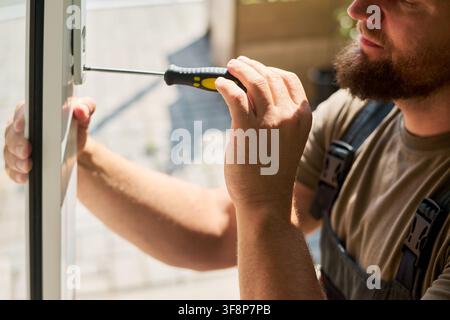 Man Repairing Window Lock with Screwdriver during Home Renovation Stock Photo