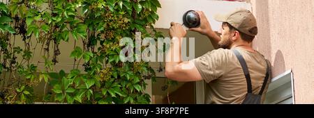 Technician Installing Security Camera on Building Wall Stock Photo
