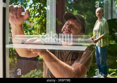 Handyman Installing Window Screen with Female Customer Watching Stock Photo