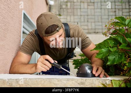 Man Installing Security Camera with Screwdriver on Building Wall Stock Photo
