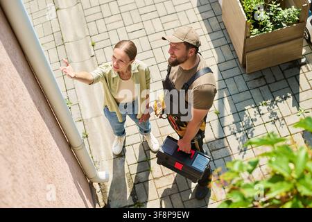 Woman Showing Gutter Problem to Handyman Holding Toolbox Stock Photo