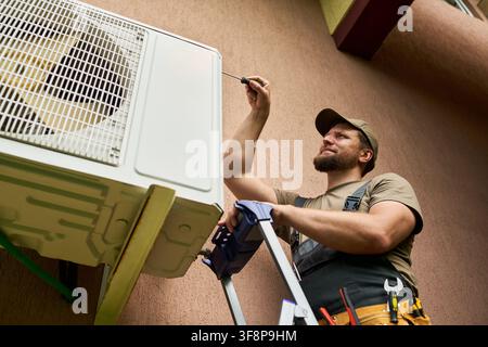 Man Fixing Outdoor Air Conditioner Unit with Screwdriver Stock Photo
