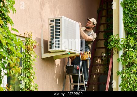 Technician Man Installing Air Conditioner Unit on House Wall Stock Photo