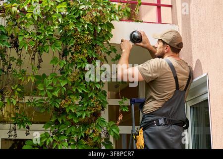 Technician Installing Security Camera on Building Exterior Wall Stock Photo