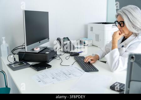 Senior doctor analyzing patient data on a workstation in a healthcare environment Stock Photo