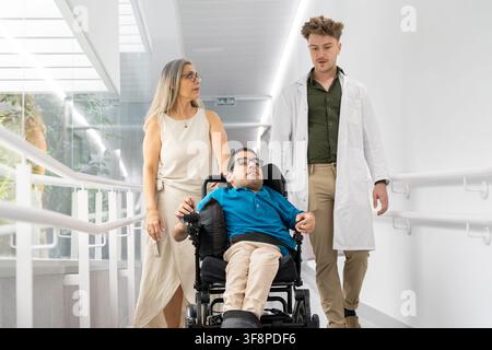 Healthcare professionals assisting a disabled man in a wheelchair along an accessible ramp Stock Photo