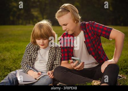 two schoolboys studying together on grass with books and smartphone in park Stock Photo