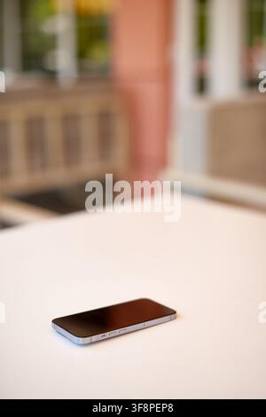 smartphone lying on white table with dark blank screen on blurred outdoor cafe background Stock Photo
