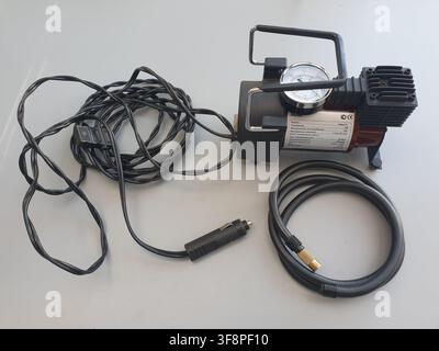 A portable car air compressor with its accessories rests on a grey surface Stock Photo