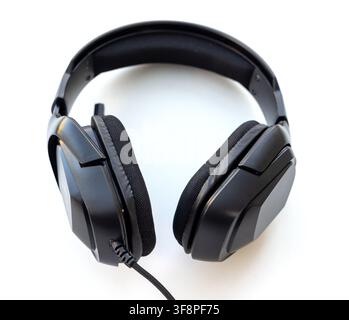 A black overear headset with a braided cable rests on white Stock Photo