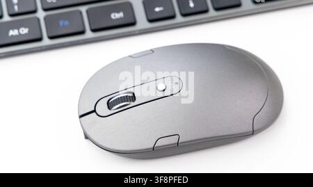 A modern grey wireless computer mouse sits next to a keyboard Stock Photo