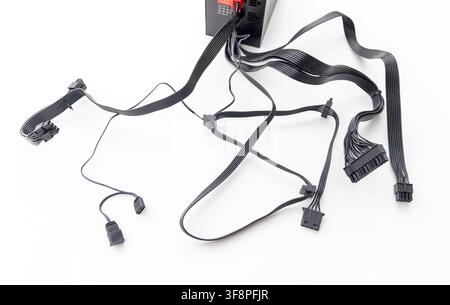 A black computer power supply unit and cables are on a white surface Stock Photo