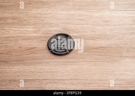 Black camera lens cap resting on textured light wooden surface with visible grain pattern Stock Photo