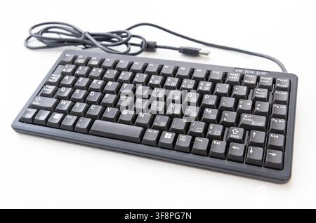 A black wired computer keyboard rests on a plain white surface Stock Photo