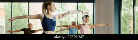 Young Caucasian female instructor leading yoga class with senior participants in modern studio, promoting active aging and wellness, medium shot Stock Photo
