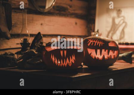 Laane County, Estonia - 31 October 2024: View of two carved jack-o'-lanterns with glowing faces resting on a rustic wooden table in a dimly lit room. Stock Photo