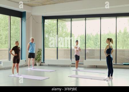 Diverse group of senior and mature Caucasian people practicing yoga with female instructor in modern studio, promoting active aging and wellness, wide shot Stock Photo