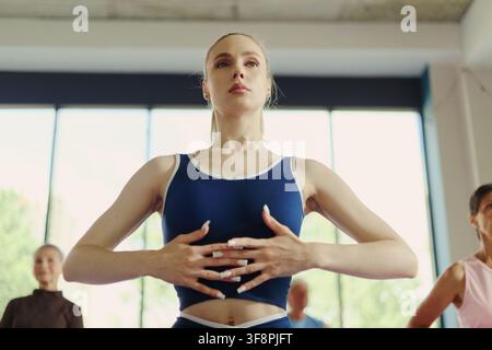 Caucasian young woman practicing breathing exercises during group yoga class in modern fitness studio, promoting mental wellbeing and healthy lifestyle, low angle shot Stock Photo