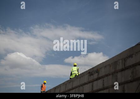 Nairobi, Kenya - 06 February 2022: View of two construction workers wearing high-visibility vests and yellow hard hats standing on a concrete wall und Stock Photo