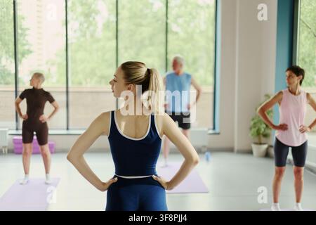 Rear view of young Caucasian woman leading fitness class for diverse group of active seniors in modern gym. Image represents healthy aging and is suitable for wellness marketing Stock Photo