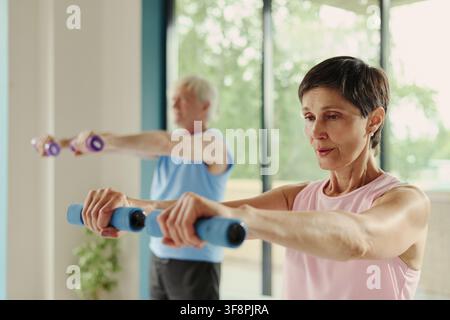 Senior Caucasian woman and man exercising with dumbbells in gym, focusing on active aging and physical health. Image suitable for senior wellness and active lifestyle marketing campaigns Stock Photo