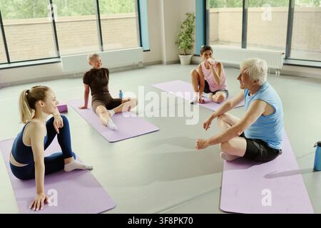 Diverse group of Caucasian senior and young people sitting on yoga mats and talking after workout. High angle view of active seniors in fitness class promoting healthy lifestyle Stock Photo