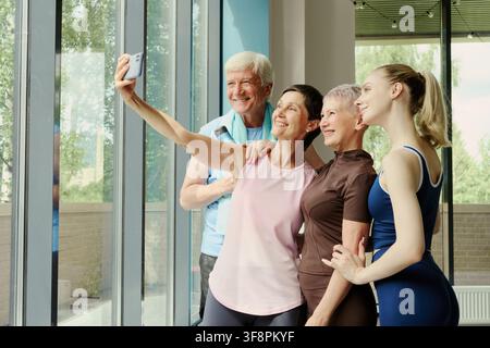 Diverse age group of Caucasian people taking selfie on smartphone in gym, smiling after workout. Image represents active lifestyle and is suitable for fitness marketing Stock Photo