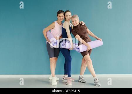 Portrait of three Caucasian women of different generations holding yoga mats and smiling. Image represents active lifestyle and is suitable for fitness and wellness marketing campaigns Stock Photo