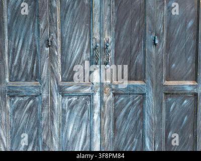 A weathered blue wooden door with textured paint strokes and rustic metal handles conveying aged charm and quiet atmosphere Stock Photo