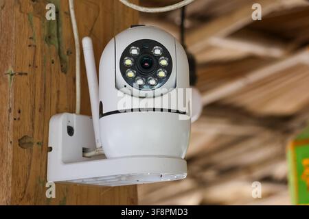 A white wireless security camera mounted on wooden beam with night leds and antenna, monitoring rustic indoor space with focused surveillance and prot Stock Photo