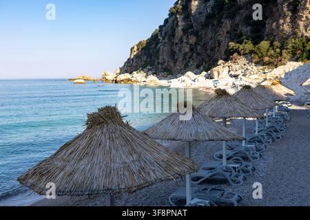 a tranquil beach scene featuring rocky cliffs and white umbrellas, set against a backdrop of a calm coastal landscape, evoking a sense of relaxation a Stock Photo
