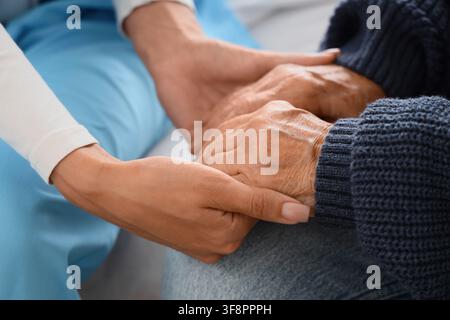 Young person holding an elderly persons hands, showing care, support, and compassion in a healthcare setting Stock Photo