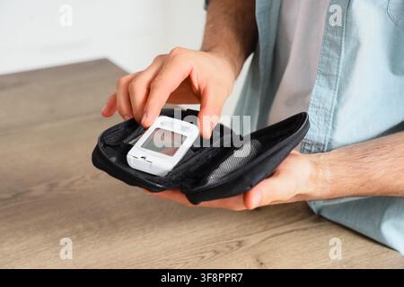 Mans hands holding a white glucose meter in a black case, diabetes management and health monitoring concept, this medical device is used for regular b Stock Photo