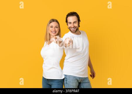 Happy Caucasian Male And Female Pointing Smiling At Camera, Yellow Background, Business Concept Stock Photo