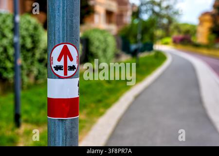 Official red and white Via Francigena waypoint sticker on a pole with arrow and pilgrim symbol, on the Parco Lineare cycle path near Appiano station. Stock Photo