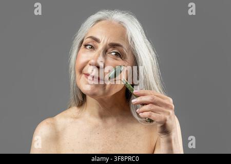 Elderly Woman Using Facial Roller On Skin, Close Up, Skincare Routine, Wellness Concept Stock Photo