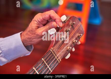 Musician hand tuning a vintage acoustic guitar string using a tuning peg Stock Photo