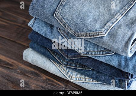 Stack of folded blue denim jeans in various shades on a dark wooden background, fashion and textile industry Stock Photo