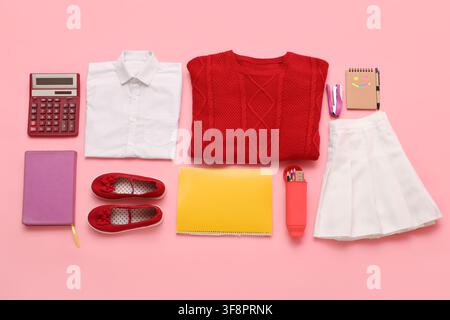 School uniform and supplies for a student including a white shirt red sweater and various stationery items on a pink background Stock Photo