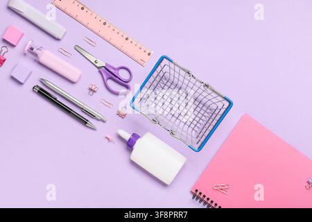 School supplies and stationery items with a miniature shopping basket on a pastel purple background, flat lay composition Stock Photo